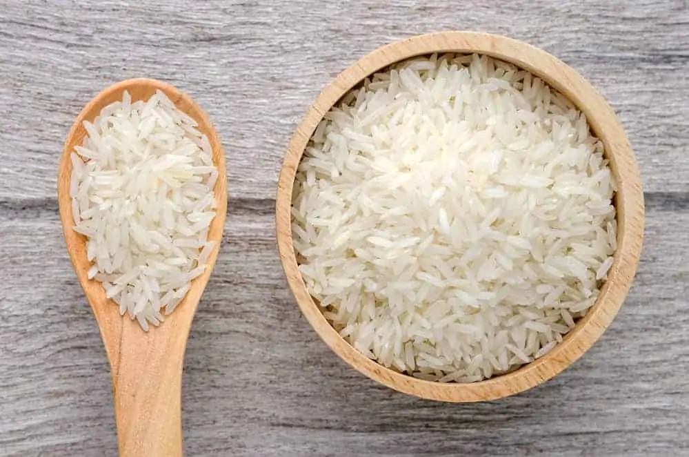 Uncooked rice in bowl on white wood background