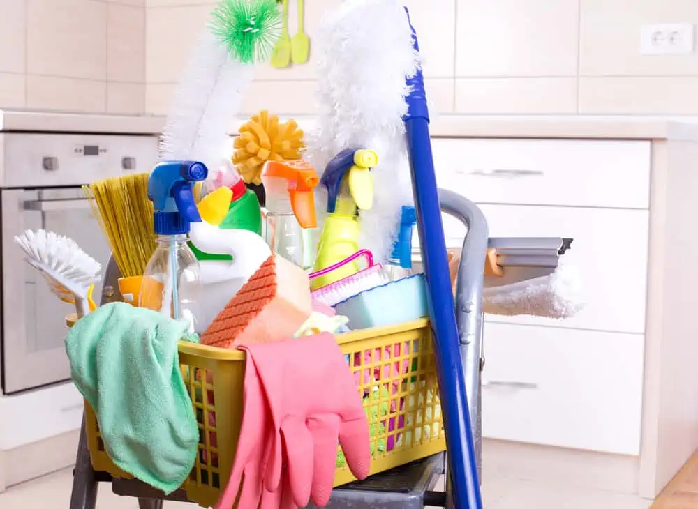 Cleaning supplies in plastic basket on ladder and mop in the kitchen
