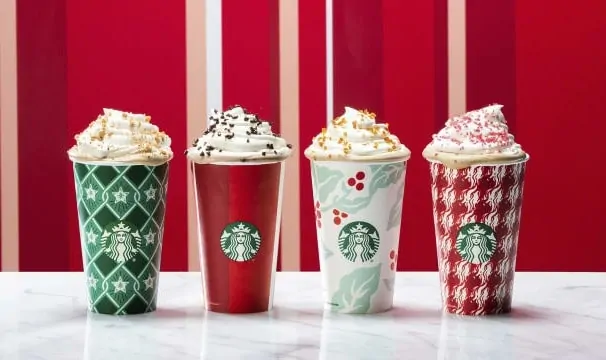 A variety of Christmas drinks in Starbucks cups with whip cream and toppings.