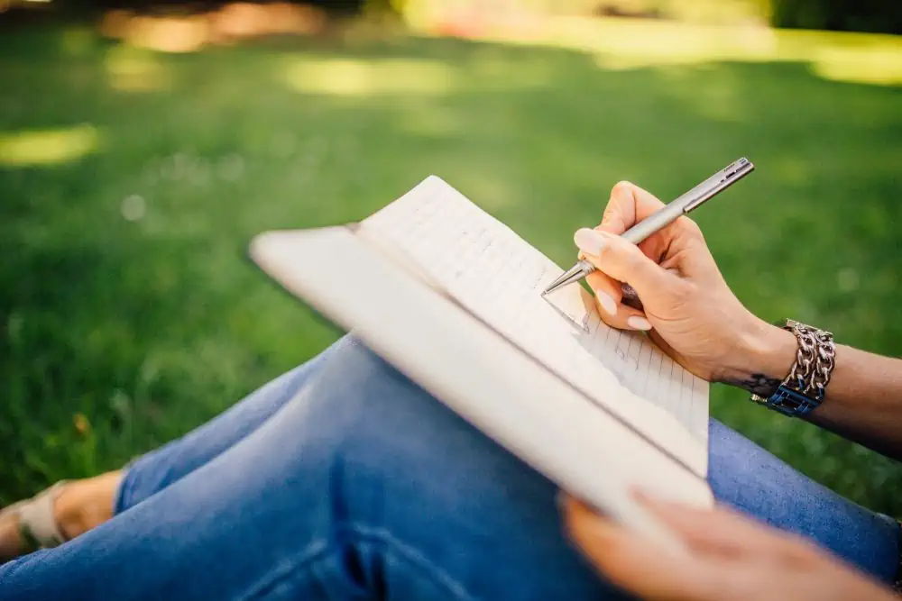 A person sitting on the grass writing in her journal.