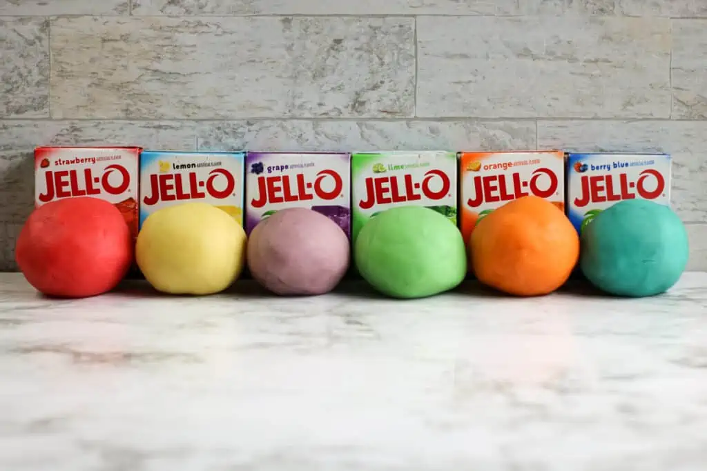 several balls of colored playdough lined up on a table with boxes of Jello