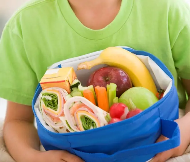 Young boy holding packed lunch in living room smiling