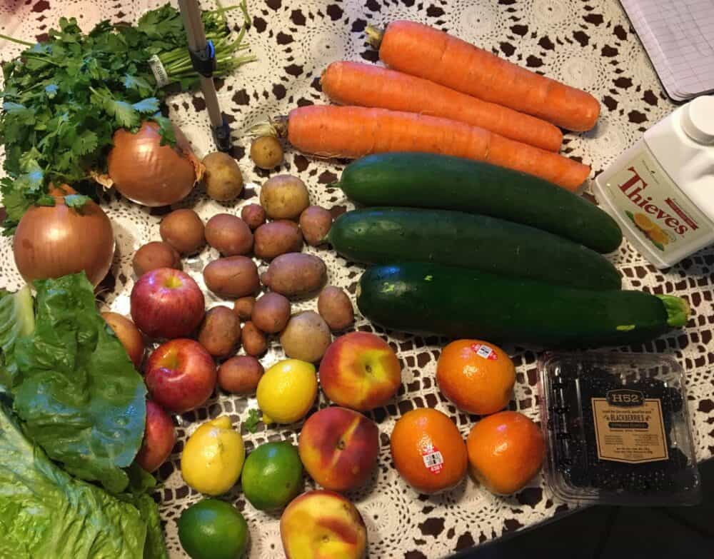 carrots, cucumber, oranges, apples, potatoes, lettuce, onions, lemons, limes and berries sitting on a kitchen table