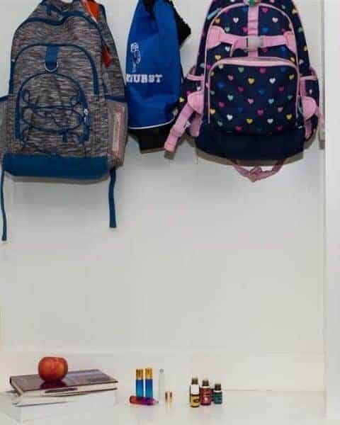 backpacks hanging in a hallway with several books, an apple and bottles of essential oils below them on a table.