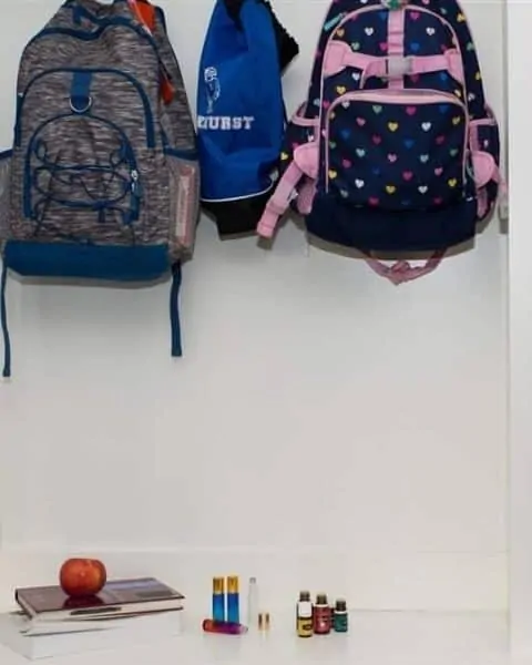 backpacks hanging in a hallway with several books, an apple and bottles of essential oils below them on a table.
