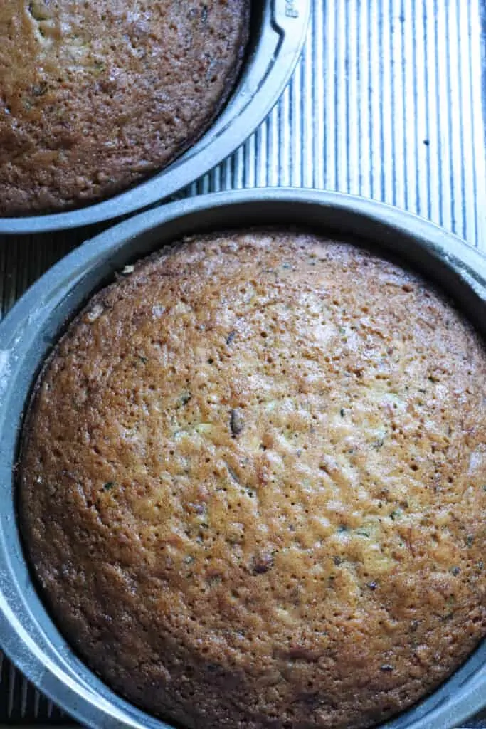 two baked zucchini cakes in round cake pans sitting on a cooling rack.