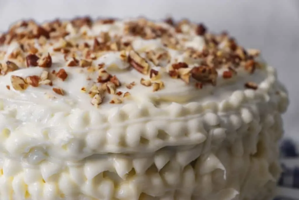 close up picture of a frosted zucchini cake with chopped pecans on top.