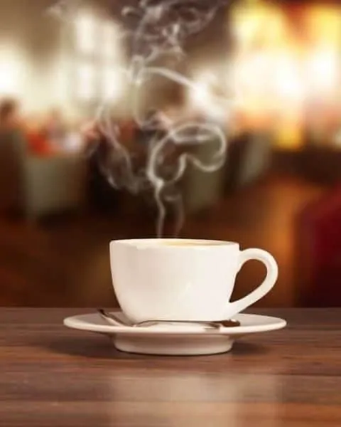 a cup of steamy coffee sitting on a wooden table.