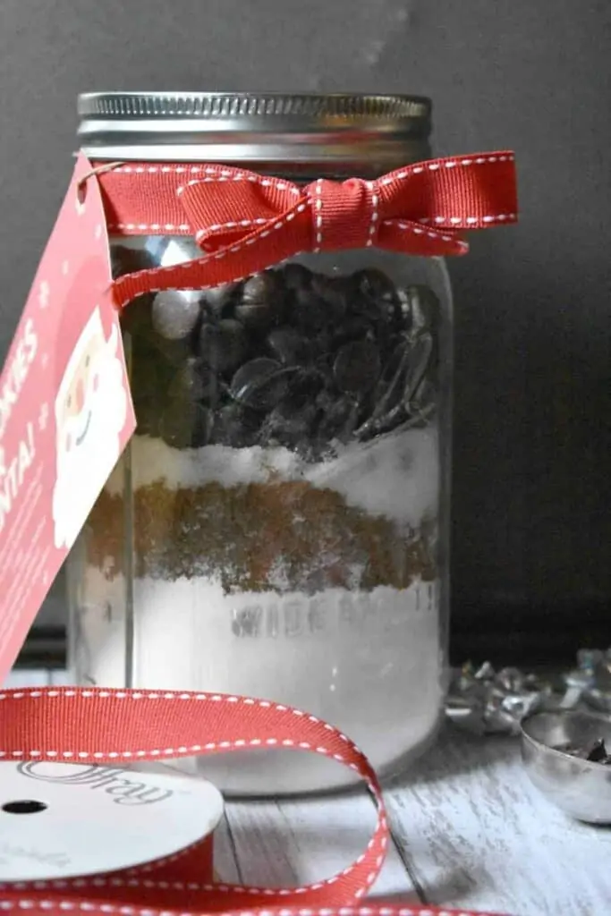 Jar with flour, sugar, and chocolate chips wrapped in a red Christmas ribbon.