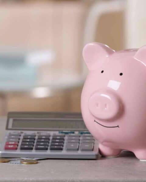 Pink ceramic piggy bank with a calculator and coins scattered.
