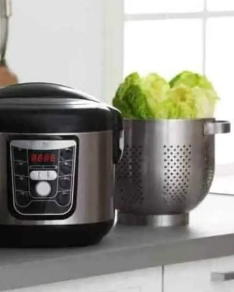 A pressure cooker next to a strainer with lettuce in the kitchen.