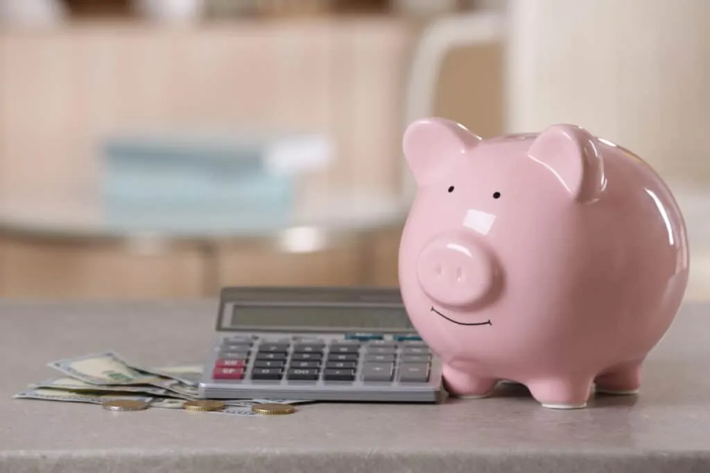 pink ceramic piggy bank sitting near a calculator and money. Saving power concept. 