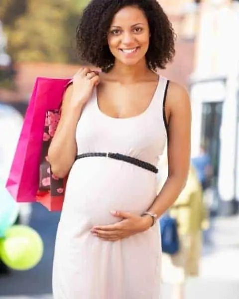 A young mother who is cradling her pregnant belly while carrying pink shopping bags.
