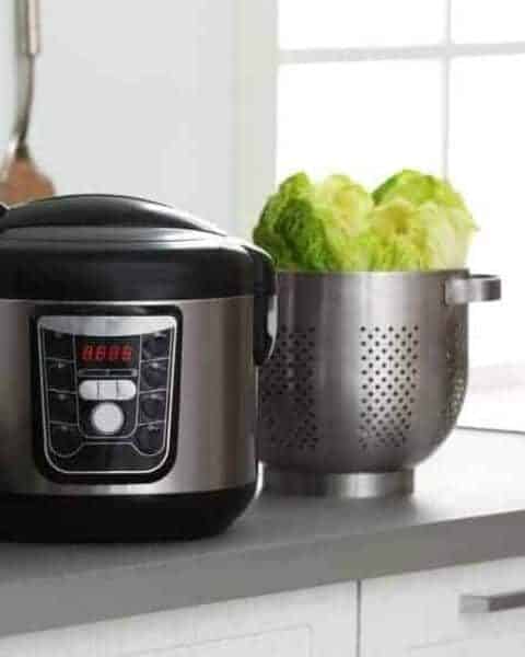 Pressure cooker on a kitchen counter with a kitchen strainer full of lettuce.