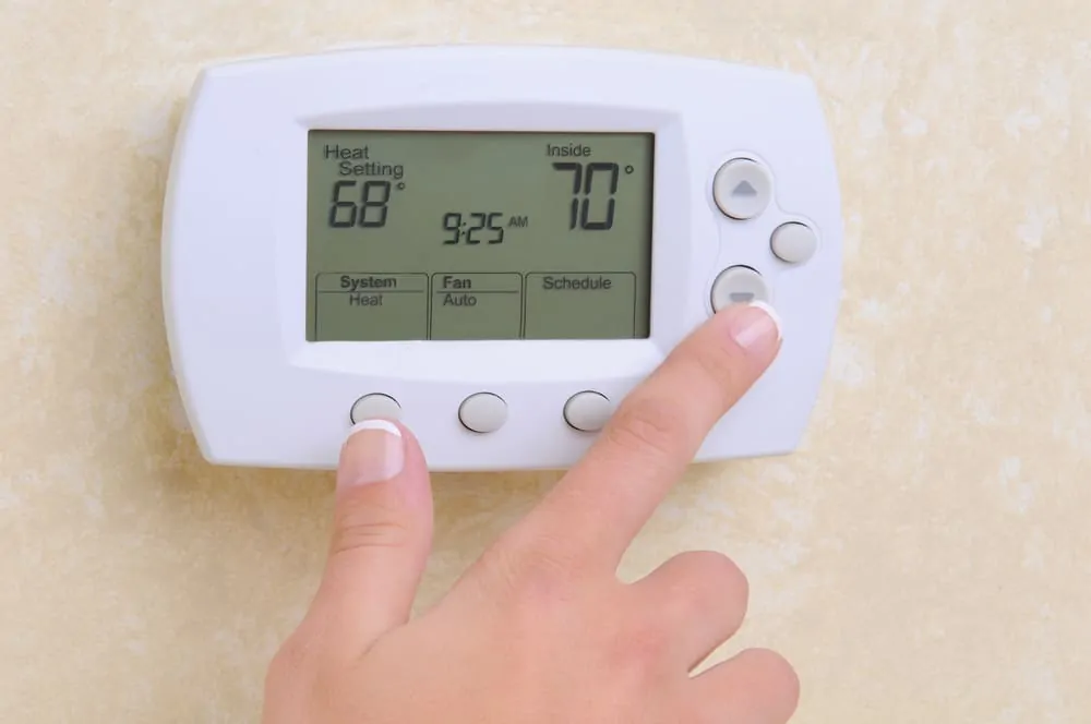 Woman adjusting the temperature setting on a programmable thermostat.