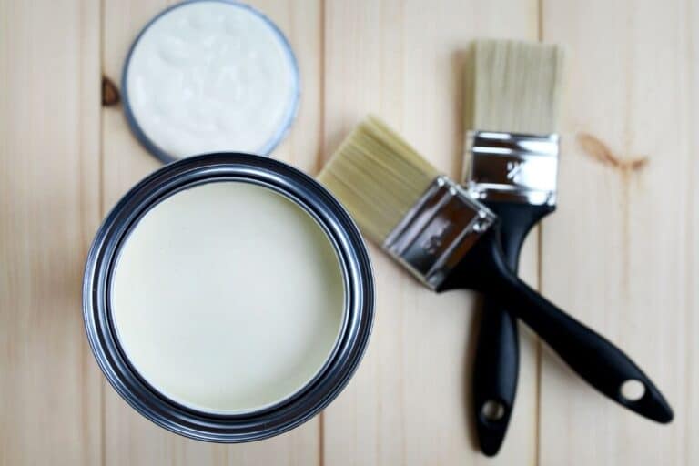 White paint opened up with two paint brushes next to the paint bucket.