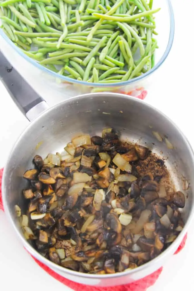 onions and mushrooms sauteed in a pan sitting near a bowl of fresh green beans