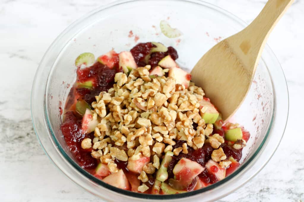 Adding chopped walnuts to a bowl of chopped apple and walnuts. 