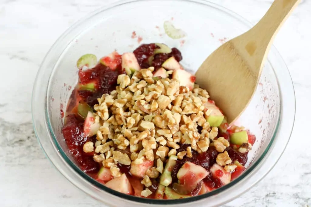 Adding chopped walnuts to a bowl of chopped apple and walnuts. 