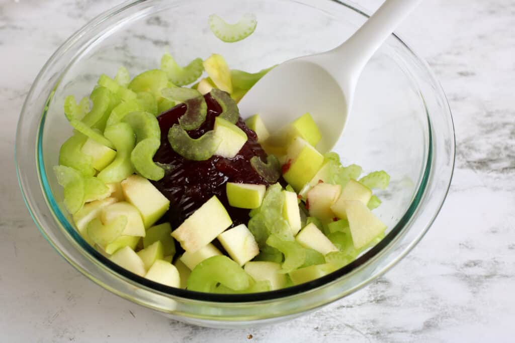 chopped apple and celery in a bowl being stirred by a spoon.