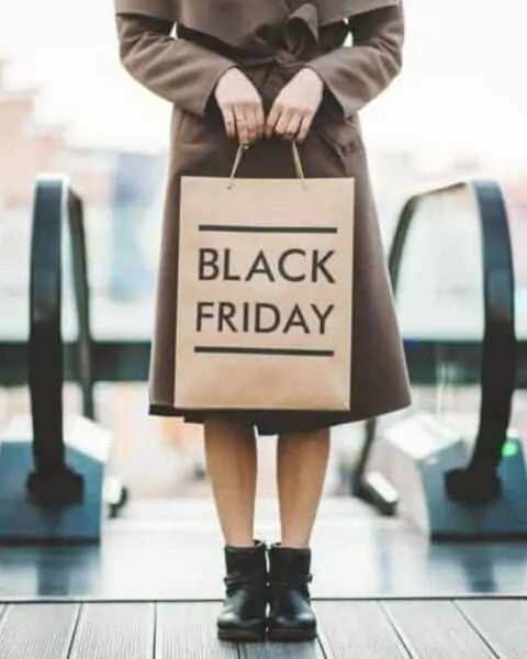 A woman wearing a brown coat holding a brown bag that reads "Black Friday."