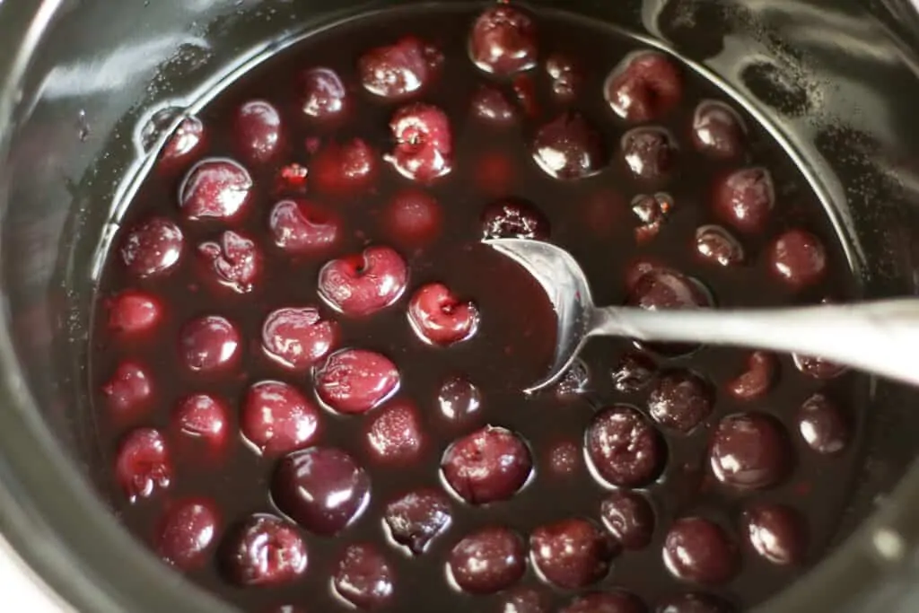 Cooked cherries soaking in sauce inside a slow cooker.