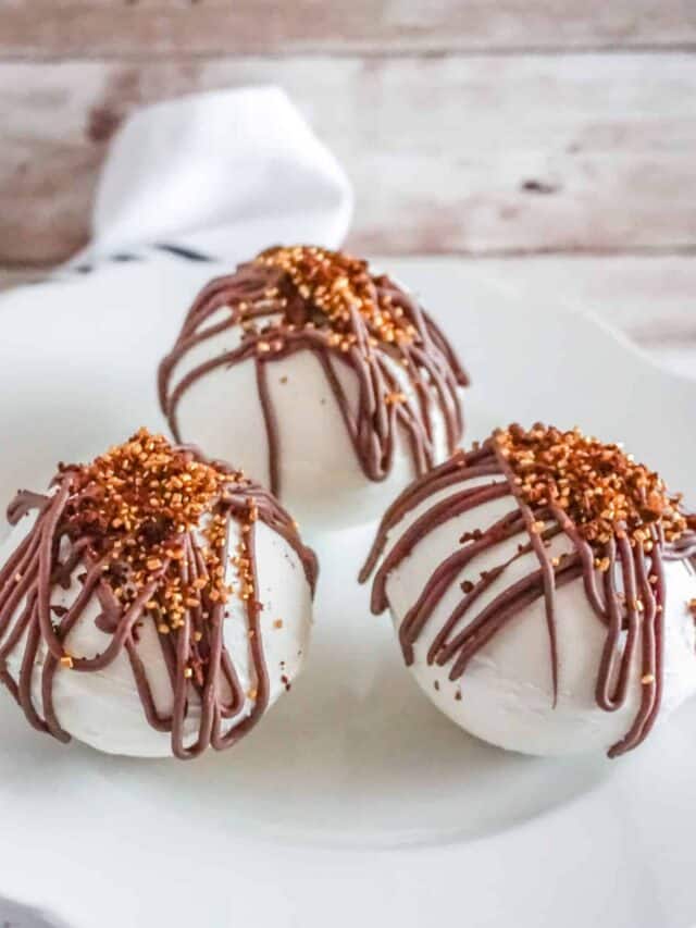Three white chocolate mocha bombs with milk chocolate drizzled on top.