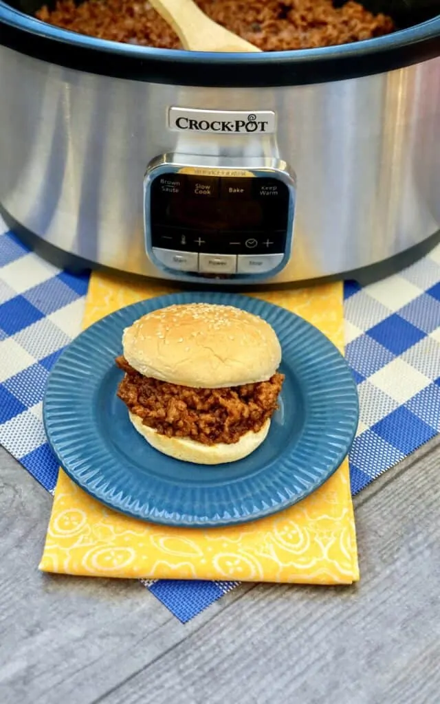 Sloppy Joe hamburger on a blue plate in front of a crock pot.