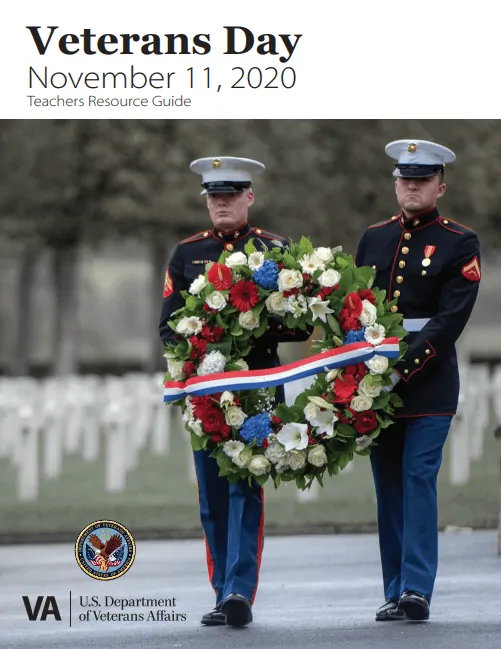 Two US Military members holding a red, white, and, blue wreath and walk together in the Veterans cemetery. 