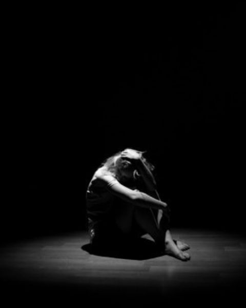 A woman sitting in the dark with her head buried in her hands.