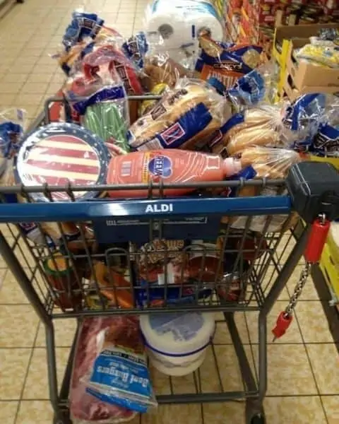 An Aldi shopping cart full of groceries, including breads, paper towels, paper plates, ice cream, and more.