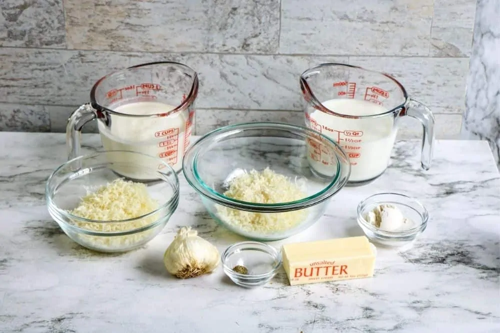 The ingredients to make alfredo sauce sitting on a countertop, including butter, garlic, cheeses, milk and heavy cream.