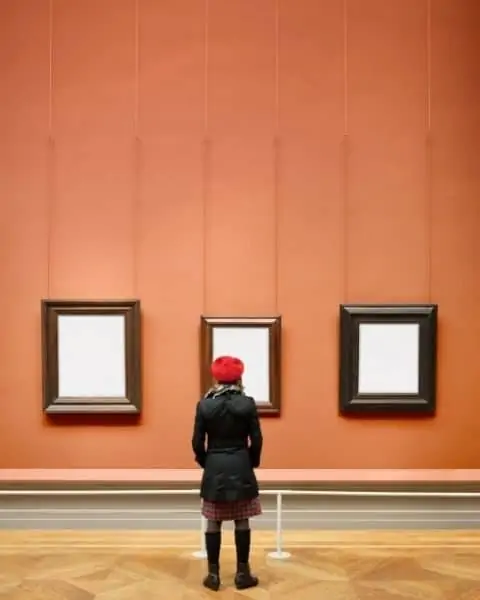 A woman looking at three framed pieces of art with blank white canvases.
