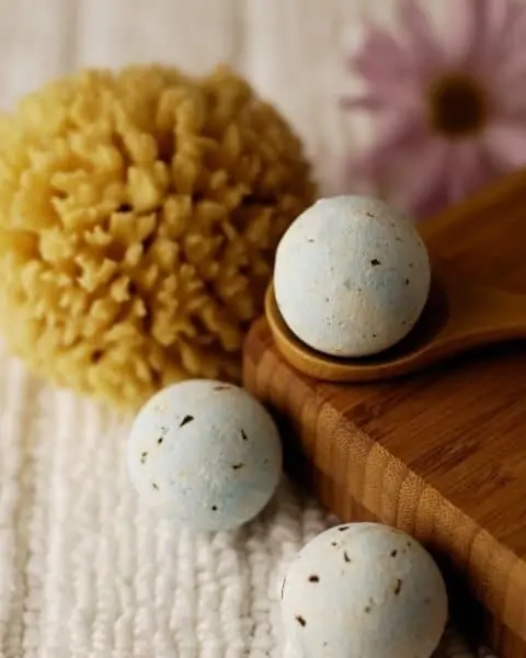 Homemade bath fizzies on wooden boards and next to bath sponges.