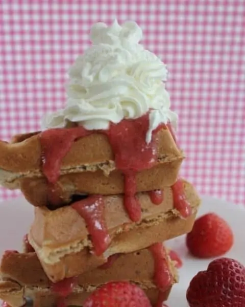 A stack of strawberry belgian waffles with whip cream.