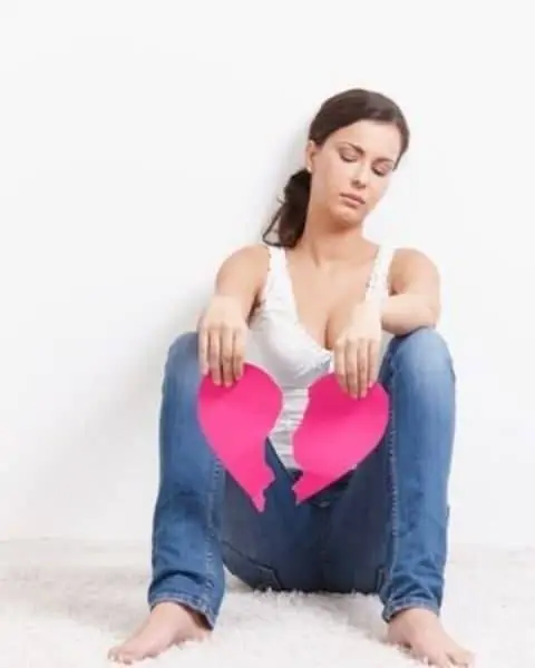 A woman sitting on the ground with a paper heart broken in two pieces.