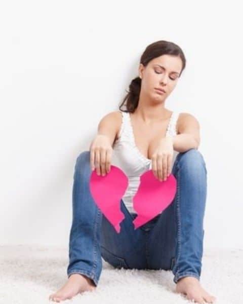 A woman sitting on the ground with a paper heart broken in two pieces.