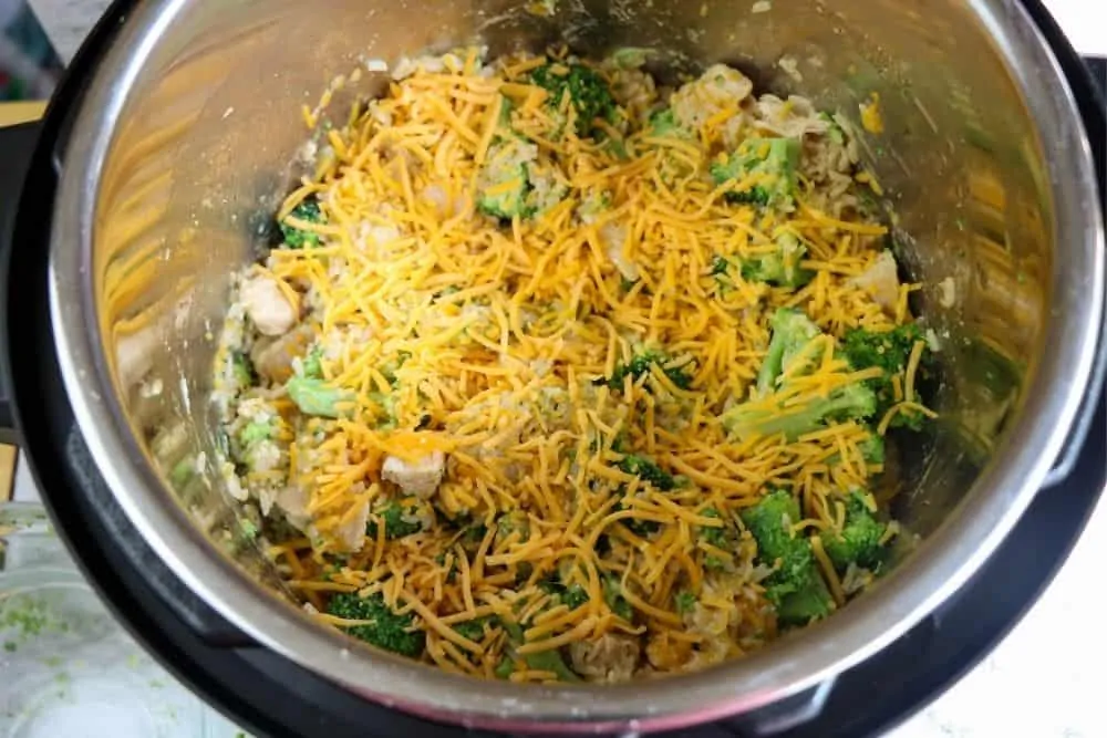 broccoli, chicken and rice covered in shredded cheese cooking inside a pressure cooker. 