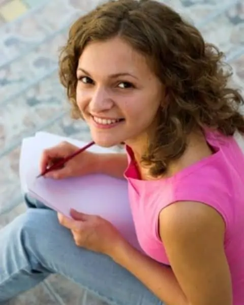 A young woman in a pink shirt writing in a notebook.