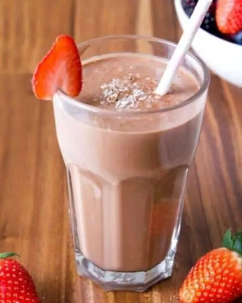 Homemade chocolate berry smoothie strawberries scattered around the drink..