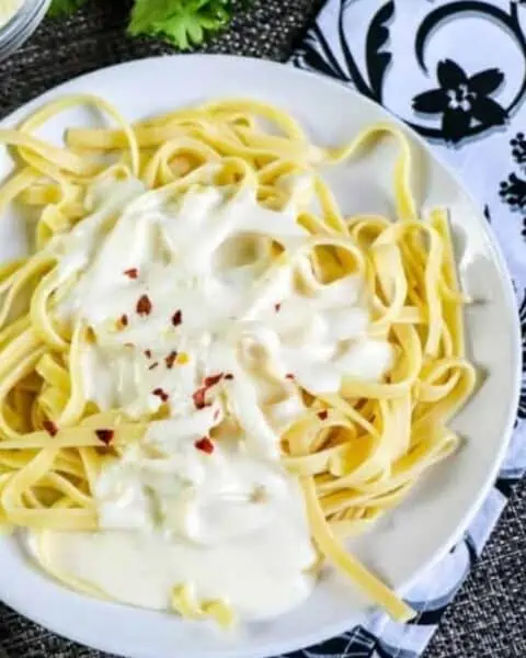 A white plate of linguini noodles with a white alfredo sauce.