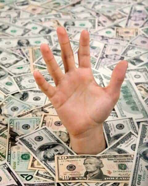 A hand reaching above a sea of money.