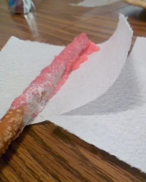 A frosting and sprinkle covered pretzel stick laying on a paper towel.