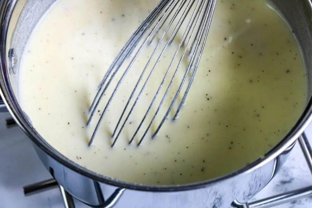 someone whisking alfredo sauce in a pan