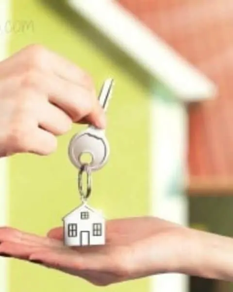 One person handing a key with a house keychain to another person after purchasing a home.