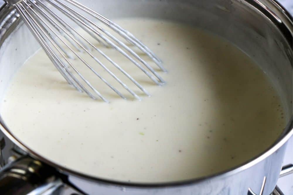 a whisk in a pan of alfredo sauce