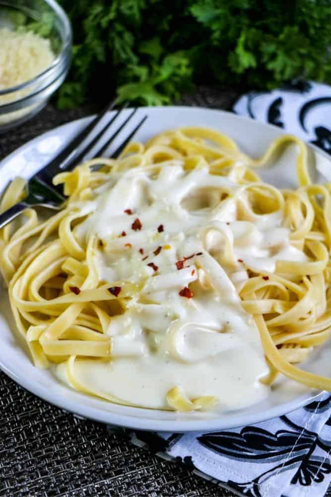 close up of garlic alfredo sauce on top of a plate of pasta.
