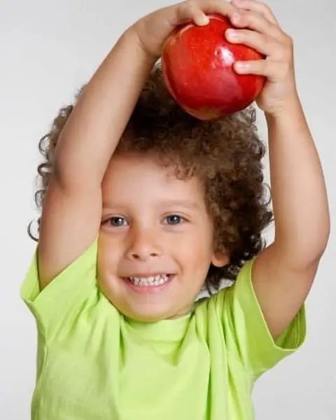 Little boy holding a red apple above his head.