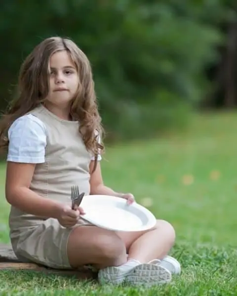 Young girl holding an empty plate with fork and knife.