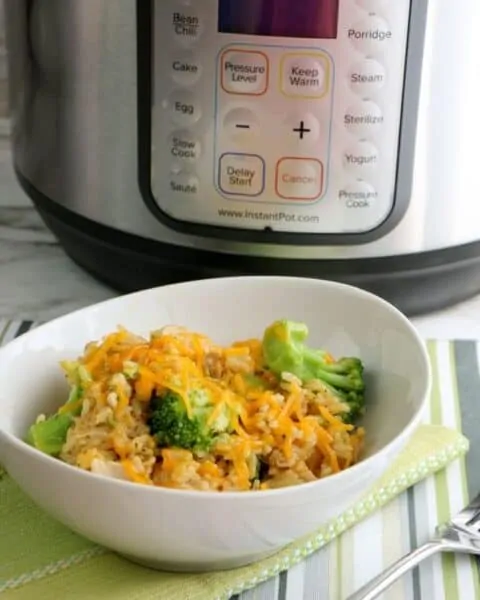 A white bowl of cheesy chicken and broccoli in front of an instant pot.